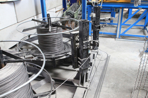  View from the back looking at the cage production line - in the foreground the coils with winding wire, behind them, on the right, the blue ESR straightening and cutting machine with the yellow attachment for the feeding of the finished longitudinal bars to the VTA 160 cage welding machine 