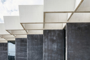  Numerous wall slabs of anthracite-colored exposed concrete, aligned parallel to each other, support a rhomboid roof structure 
