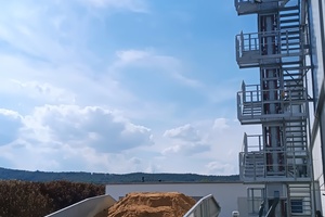  On the left, the VHV FlatFeeder with its partially heavy-load-supportinggrids. It was installed and commissioned at Weser-Diemel-Beton in March 2022. Behind it: the stairway at the dual-belt conveyor, assembled from the modular system typical for VHV  
