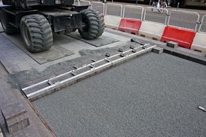  Work on the bicycle lane: following screeding of the bedding, the paving slabs were installed with the aid of a jointing tool. Load-distribution plates below the heavy machine protect the freshly laid pavement from point loading. Slotted channels and transition blocks are installed to the left and right 